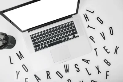 Imagem mostrando um laptop sobre uma mesa com letras recortadas ao redor, ideal para discutir SEO para Copywriting.